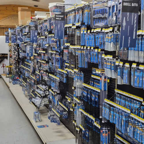 A hardware store aisle filled with various drill bits and masonry drills in blue packaging, neatly arranged on shelves and hooks, creating an organized, industrious atmosphere.