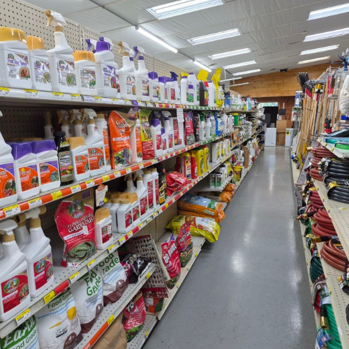 A store aisle filled with gardening supplies, including fertilizers, soil bags, and tools. Shelves are neatly stocked, creating an organized, vibrant scene.