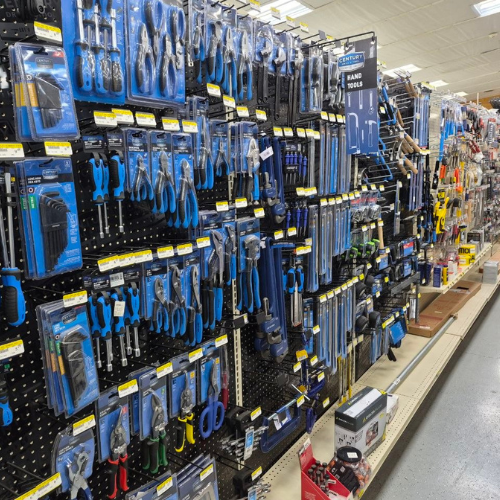 A hardware store aisle displaying a variety of hand tools like pliers, screwdrivers, and wrenches in blue packaging on a pegboard wall.